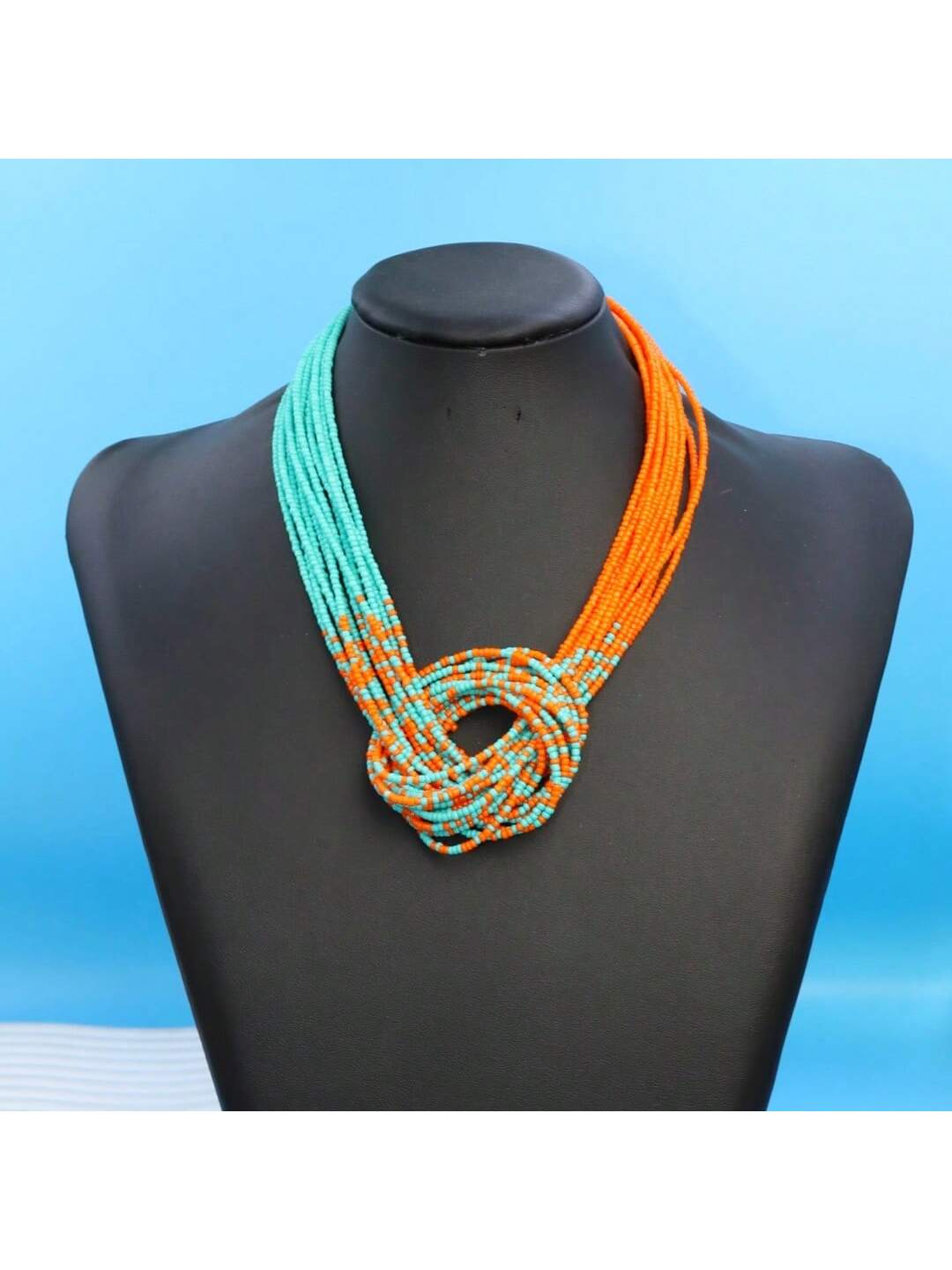 Necklace with turquoise and orange strands on a black mannequin against a blue background